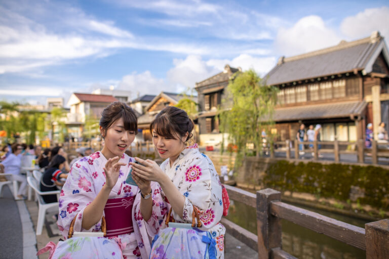 Young sisters in yukata using smart phone at traditional Japanese festival